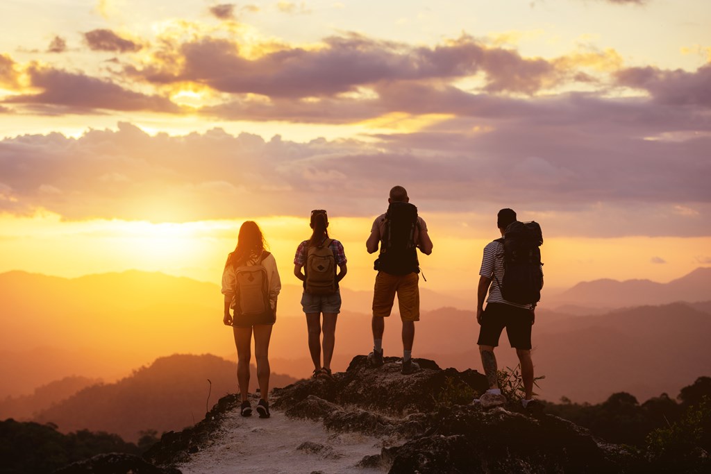 Group of four hiker's silhouettes stands on mountain top looking at the sunset.