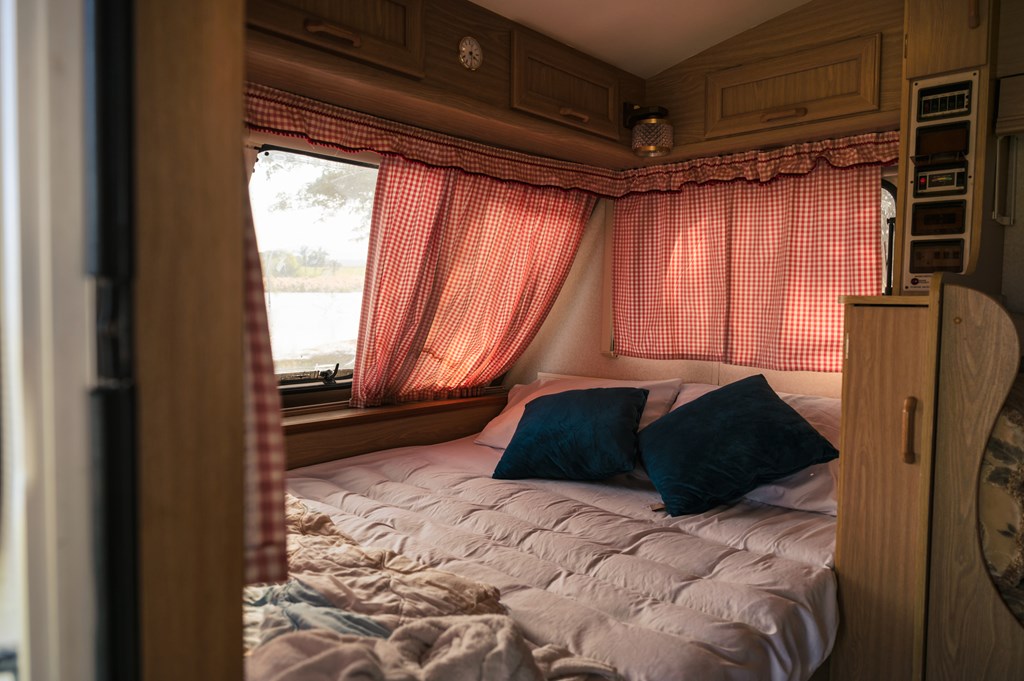 Photo of interior of a camper van with a bed, pillows, and curtains in the daytime.